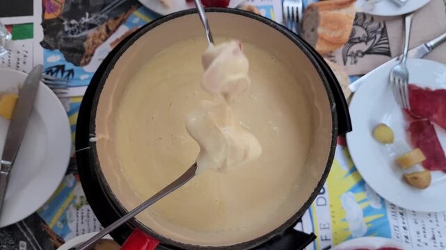 Top down view of friends sharing traditional Swiss cheese fondue dipped with bread