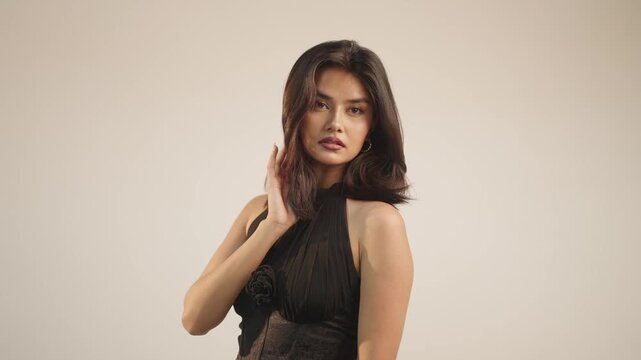 Fashion model running fingers through wavy hair in profile pose with wide negative copy space beside her in bright minimalist studio setting
