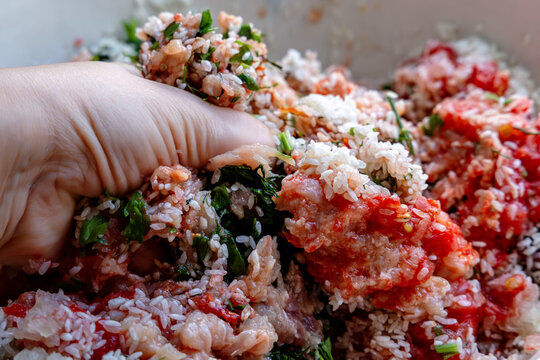 Hand mixing minced meat with rice and herbs in bowl