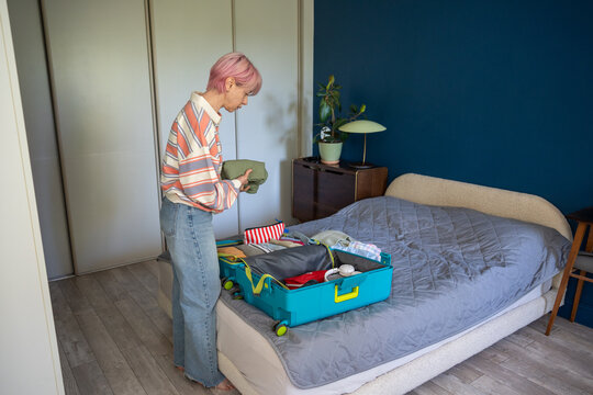 Focused woman packing suitcase for business or weekend holiday trip, putting clothes in travel case, anticipation and mindful organization, thoughtful female at home preparing baggage for vacation.