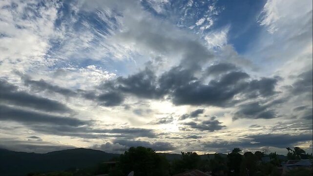 A cinematic time-lapse shot capturing dense, fast-moving clouds across the sky, partly covering the bright sun over the hilly landscape of Haflong, Dima Hasao, Assam, India. 4K UHD