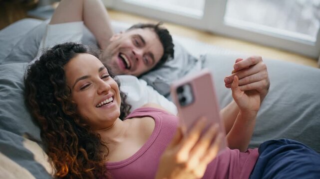 Couple relaxing bed morning browsing pink phone together. Close up weekend home