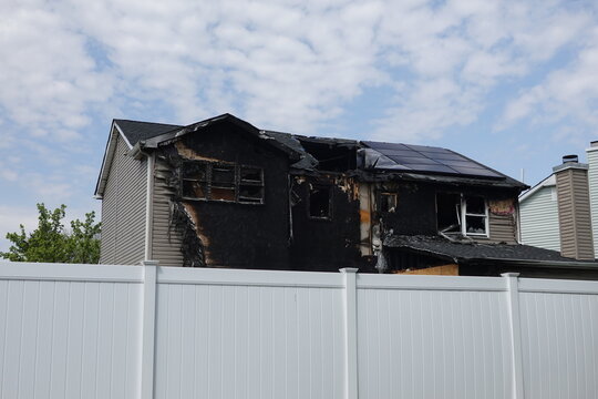 Back view of an abandoned fire damaged destroyed house with charred and melted vinyl siding atmosphere conveys disaster, neglect and damage.