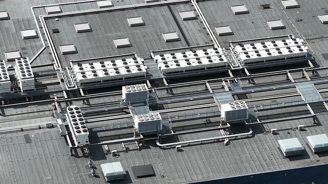 Aerial view of a large industrial building roof featuring multiple hvac cooling units, ventilation systems, and rooftop equipment on a flat grey surface
