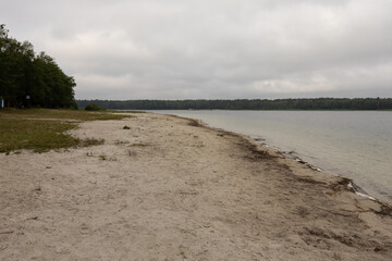 plaża nad jeziorem widok na piaszczystą plażę. Jezioro otoczone lasem jest po prawej stronie © workszop