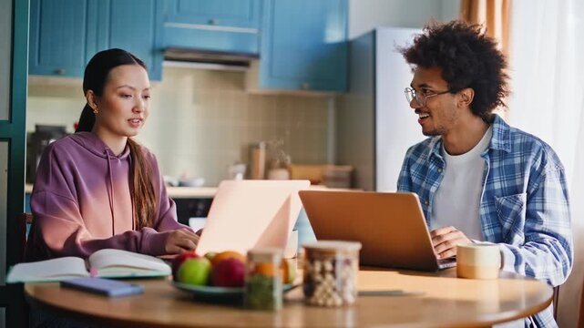 Couple working laptops at kitchen table. Multiethnic students studying home.