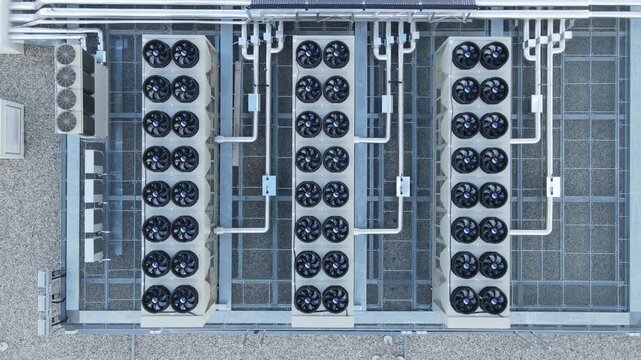 Aerial view of a large industrial hvac cooling system on a rooftop, featuring multiple rows of fans and complex piping infrastructure for climate control