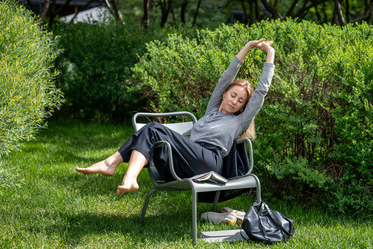 Satisfied woman resting on grass, enjoying warm weather, fresh air, open area. Relaxed female chilling, lazing, idle, gains strength. Calm quiet lady recreating on lawn in front of house