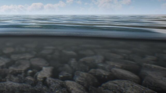 The clear water above the rocky seabed with visible stones. Soft waves move gently across the surface. The sun is shining and clouds are in the sky.