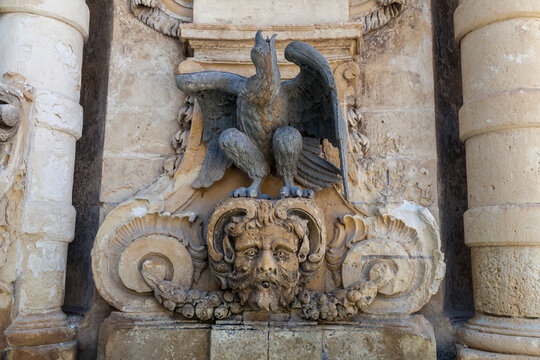 An ornate fountain with carved eagle and mascaron face in baroque stone facade detail flanked by columns in St George's Square, Valletta, Malta