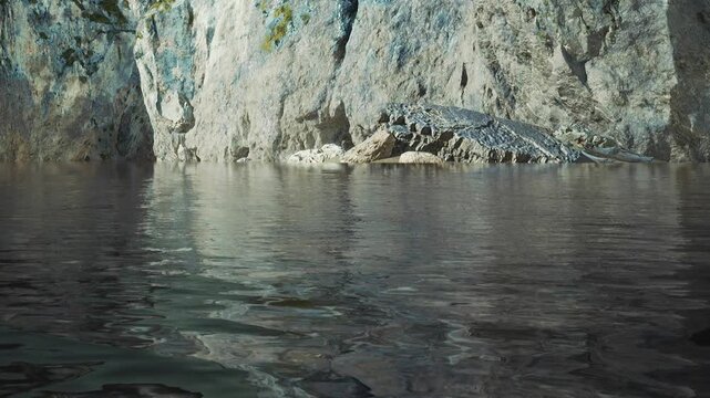 Bright sunlight shines on the water as it reflects the rocks along the shoreline. The rocky cliffs stand tall above the calm water. This scene captures the natural beauty of the coast.