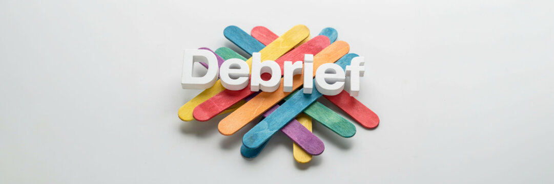 Wooden debrief sign composed of colorful popsicle sticks on white background.