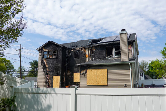 Back view of an abandoned fire damaged house with boarded windows and and doors in suburban setting
