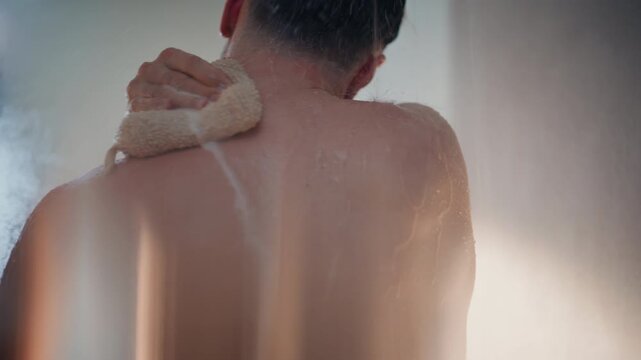 Man washing back with loofah sponge in shower. Close up rear view of bathing