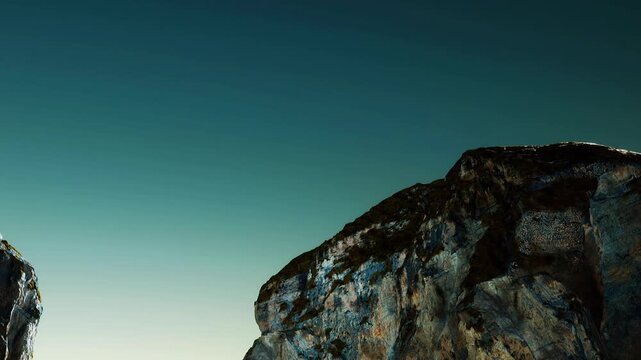 Two cliffs stand against a clear sky during the evening. The sunlight creates a soft glow on the rock formations, showing their texture and shapes. The scene captures natures beauty.