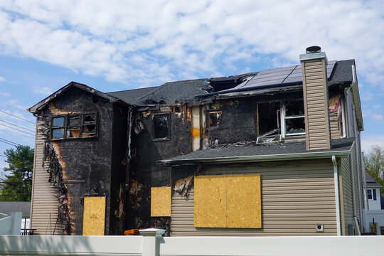 Back view of an abandoned fire damaged house with boarded windows and and doors in suburban setting