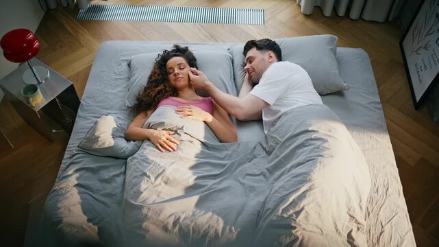 Couple waking up morning bed. Man caressing girlfriend face holding hands top