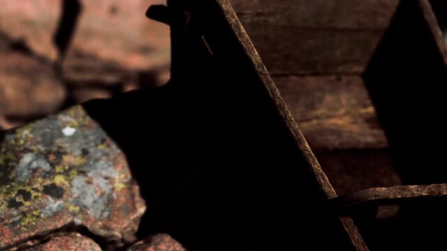 A close view captures a rusty metal object placed on a stone surface. The sunlight creates shadows around the structure. Rocks and wood are nearby, indicating an outdoor setting.
