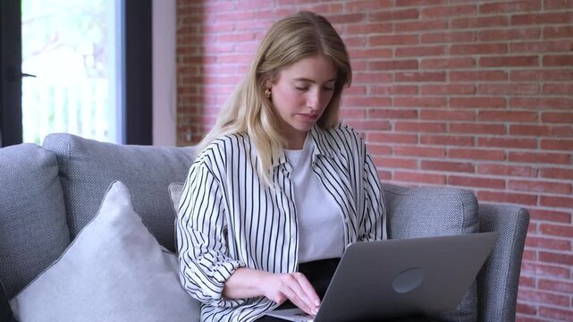 A young blonde woman is focused on her laptop on a couch at home. She reacts with surprise and frustration to an issue, then closes the device, looking thoughtfully into the distance, perhaps contempl