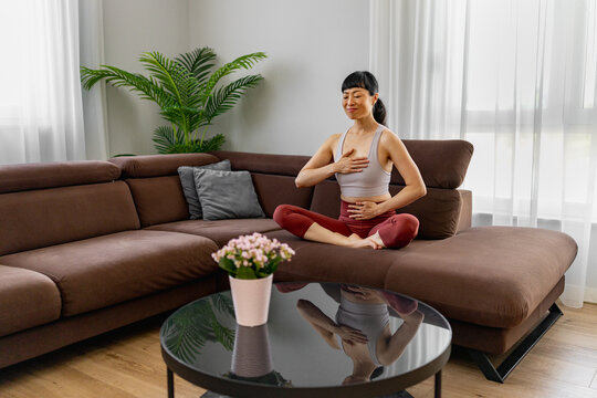 Japanese woman practicing mindful breathing and meditation in living room for relaxation and wellness