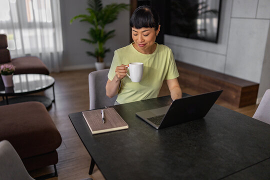 Japanese woman working from home with laptop and coffee in modern living room