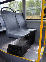 Empty city bus seats beside yellow handrails and raised platform © Daria