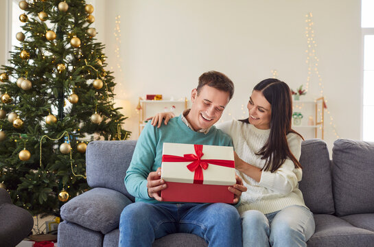 Married couple opening gift boxes at home on a festive morning, celebrating New Year or Christmas. The holiday season brings them joy as they unwrap presents in cozy family environment.