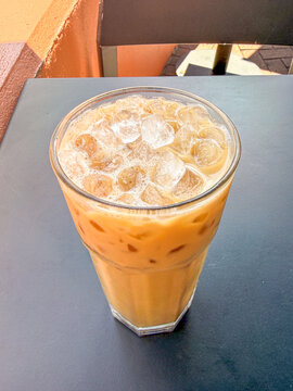 Overhead view of iced coffee in a glass with ice cubes on a dark cafe table.