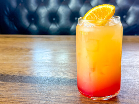 Colorful orange and red iced drink with orange garnish on a wooden restaurant table with open copy space.