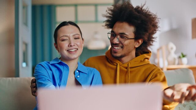 Couple watching laptop screen on sofa at home. Closeup video call reaction.
