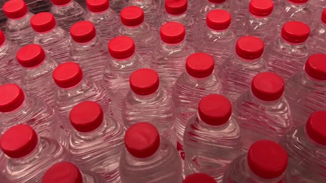 Rows of small plastic water bottles with blue and red caps displayed on store shelves. Close-up of packaged bottled drinking water in a retail supermarket beverage section