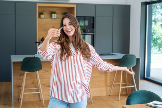Smiling young woman holding house keys in modern kitchen, celebrating new home ownership and moving day with excitement and pride. Casual lifestyle, interior, real estate, and happy homeowner concept.