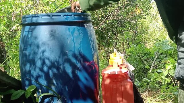 Preparing liquid herbicide in a large blue plastic drum for weeding in the plantation
