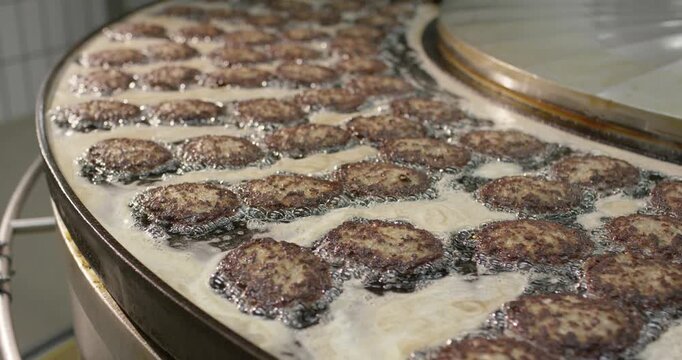 Meat patties frying in hot fat in a large industrial fryer
