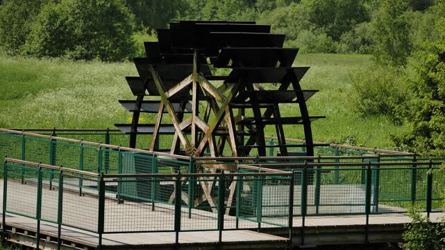 Water wheel rotating, generating renewable energy in a green park environment