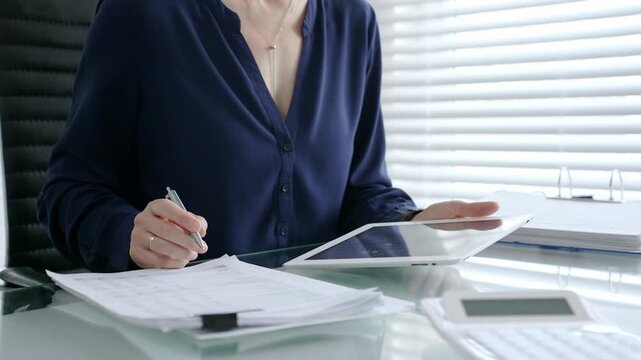Businesswoman working on a tablet, analyzing financial data and electronic documents at a modern office desk, using digital technology for accounting and management tasks