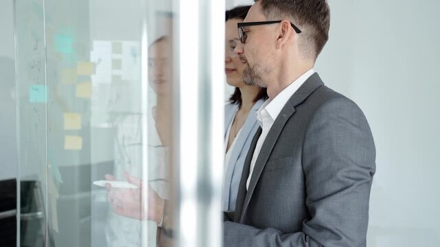 Business team collaborating on strategy, brainstorming ideas with post it notes on a glass board during an office meeting, planning effective project development