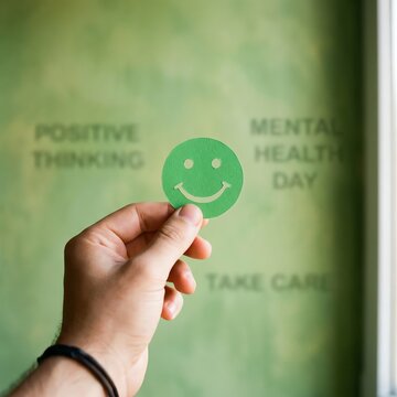 Hand holding green smiley face icon, promoting positive thinking and mental health awareness