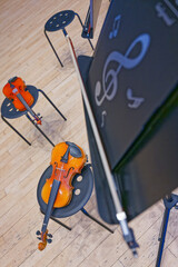 Two violins resting on black stools near a music stand with musical notes © Holger