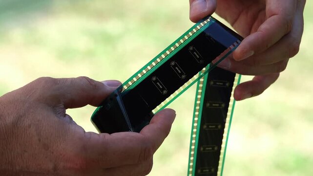 Hands holding a strip of 35mm film with perforations and sprockets. Close-up of two hands carefully handling a length of vintage 35mm motion picture film, showing the sprocket holes and perforations