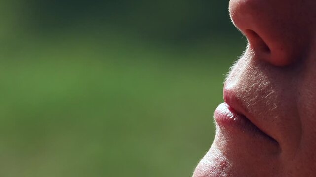 Close-up of a person exhaling a visible plume of vapor or steam. A detailed profile view captures the moment of exhalation, showing vapor dissipating into the air with a blurred green background