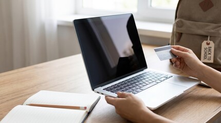Fototapeta premium Young female student shopping online for school supplies using a credit card and laptop at home desk, preparing for back to school season with digital payment technology