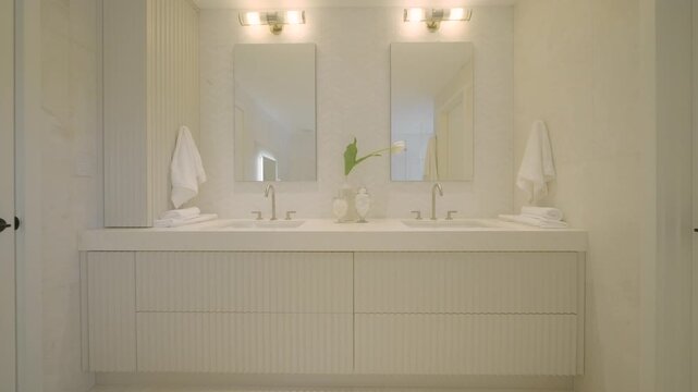 Bathroom looks clean and soft with white sinks and beige cabinet. Oval mirrors and flowers add calm touch. Light tones and smooth lines make space feel fresh