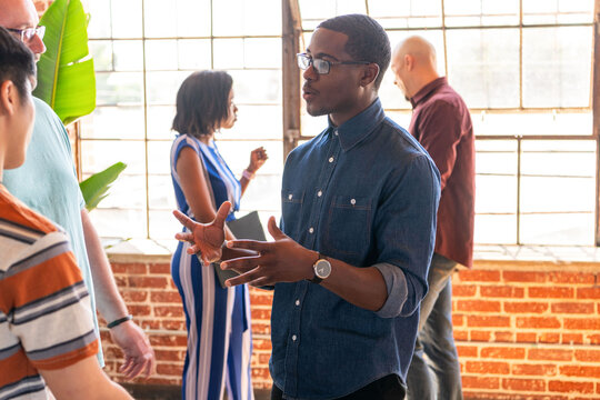 Diverse group of people engaged in conversation by large windows.