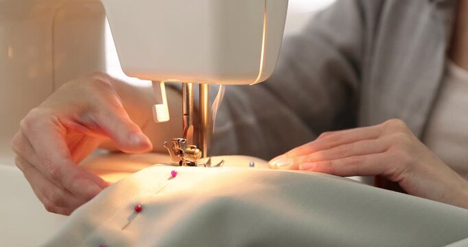 Woman sewing fabric with professional machine at table in workshop, closeup