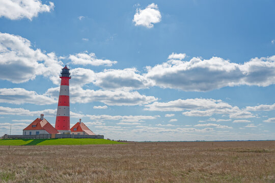 Red and white striped lighthouse with houses on grassy field under blue sky and clouds