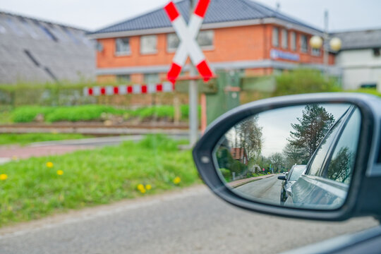 Car side mirror reflecting road and vehicles near railway crossing with warning sign
