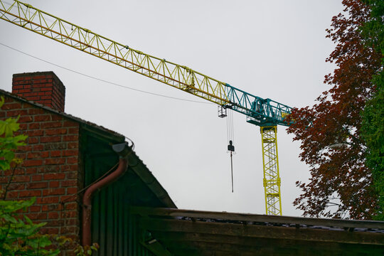Yellow and blue construction crane towering over a brick building with autumn trees