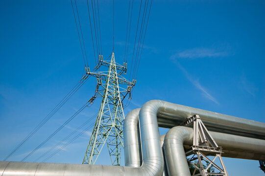 The photo shows a pipeline and a power transmission tower against a blue sky