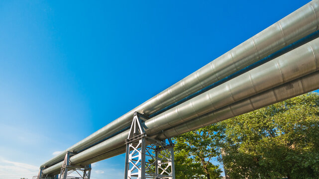 The photo shows a pipeline on metal supports against a blue sky